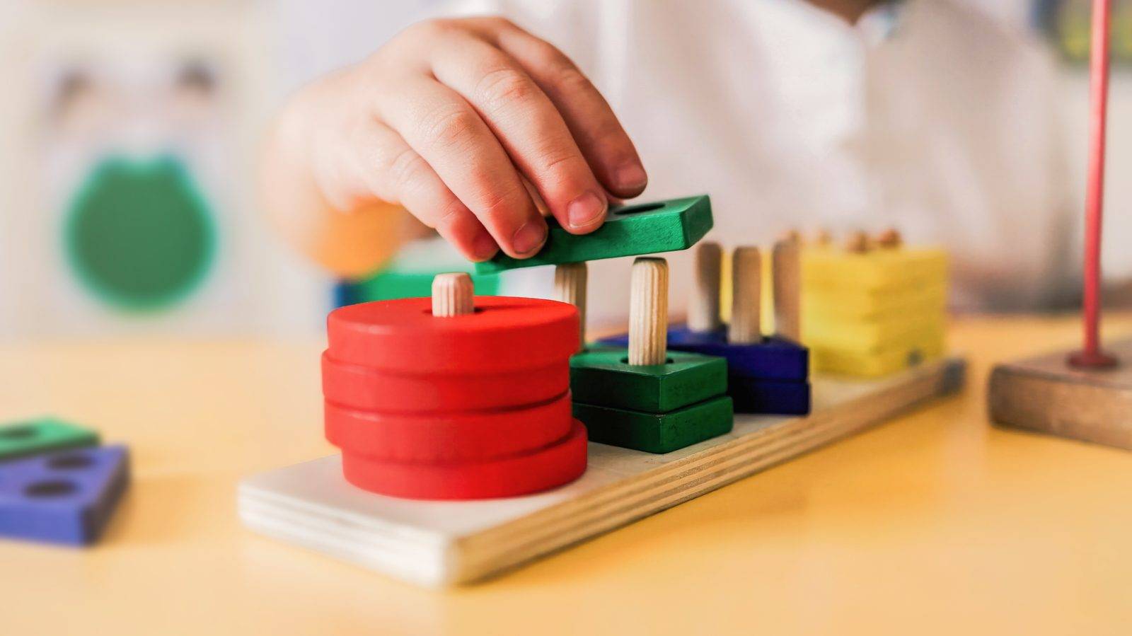 A child's hand stacking colored wooden shapes on a peg toy
